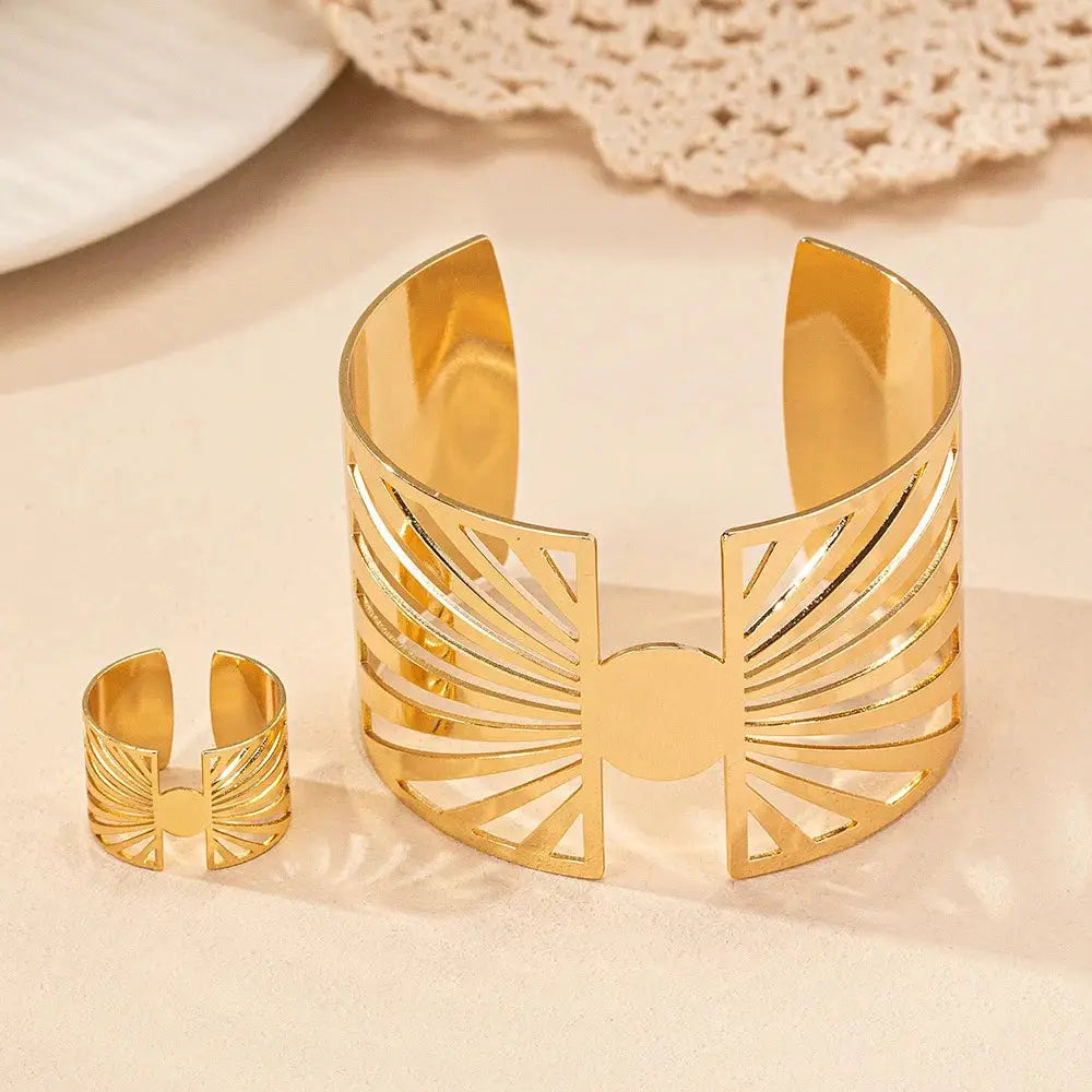 Front view of gold cut-out geometric bracelet and matching ring standing upright on a soft beige surface