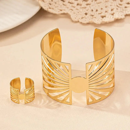 Front view of gold cut-out geometric bracelet and matching ring standing upright on a soft beige surface