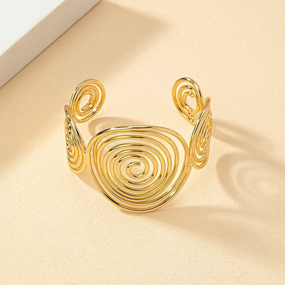 Gold geometric spiral hair cuff with shiny metallic finish, displayed on a beige surface at an angle