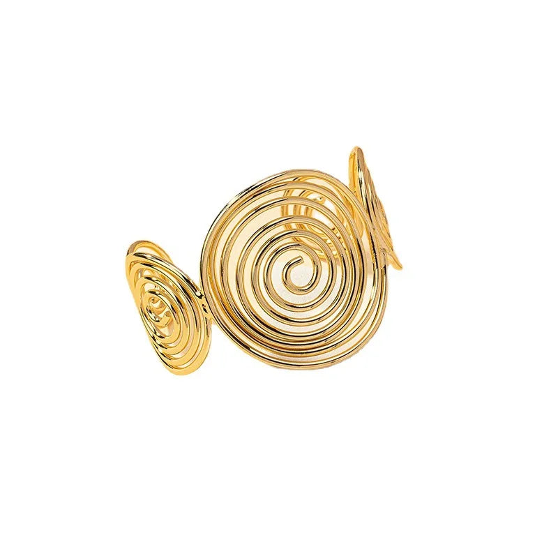 Gold geometric spiral hair cuff with shiny metallic finish, displayed on a beige surface at an angle