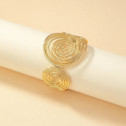 Gold geometric spiral hair cuff displayed flat on a cylindrical roll, showcasing spiral detailing.
