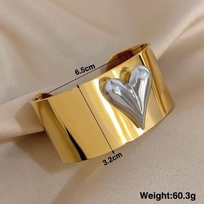 Close-up of a gold wide band cuff bracelet with measurements shown and a silver raised heart accent. The braclet is 6.5 cm wide and 3.2 cm Tall.