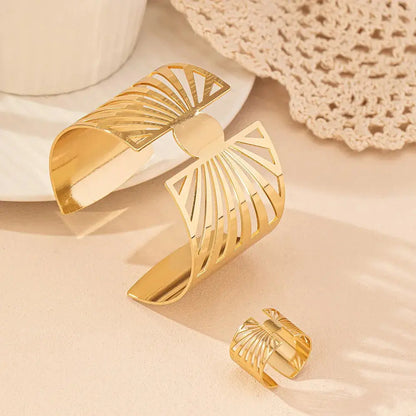 Gold geometric cut-out bracelet and matching ring displayed on a neutral background in soft lighting