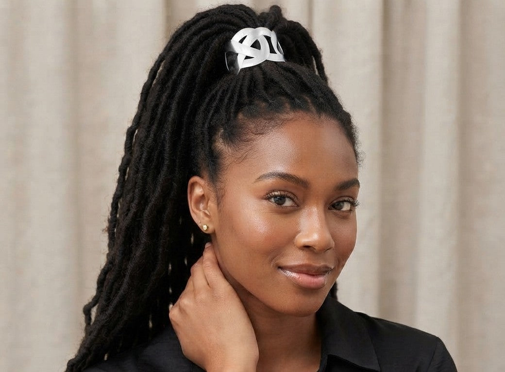 Woman with locs in a high ponytail wearing a silver interlocking-loop hair cuff, with her hand resting at her neck.