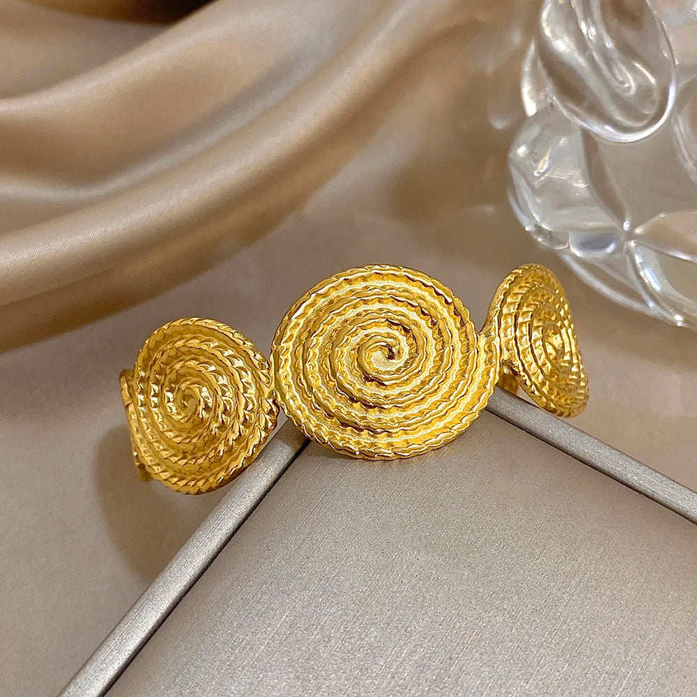 Gold hair cuff with bold spiral textured design, displayed on a neutral satin background.