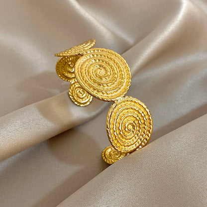 Gold spiral textured hair cuff with a layered circular design, shown at an angle on satin fabric.