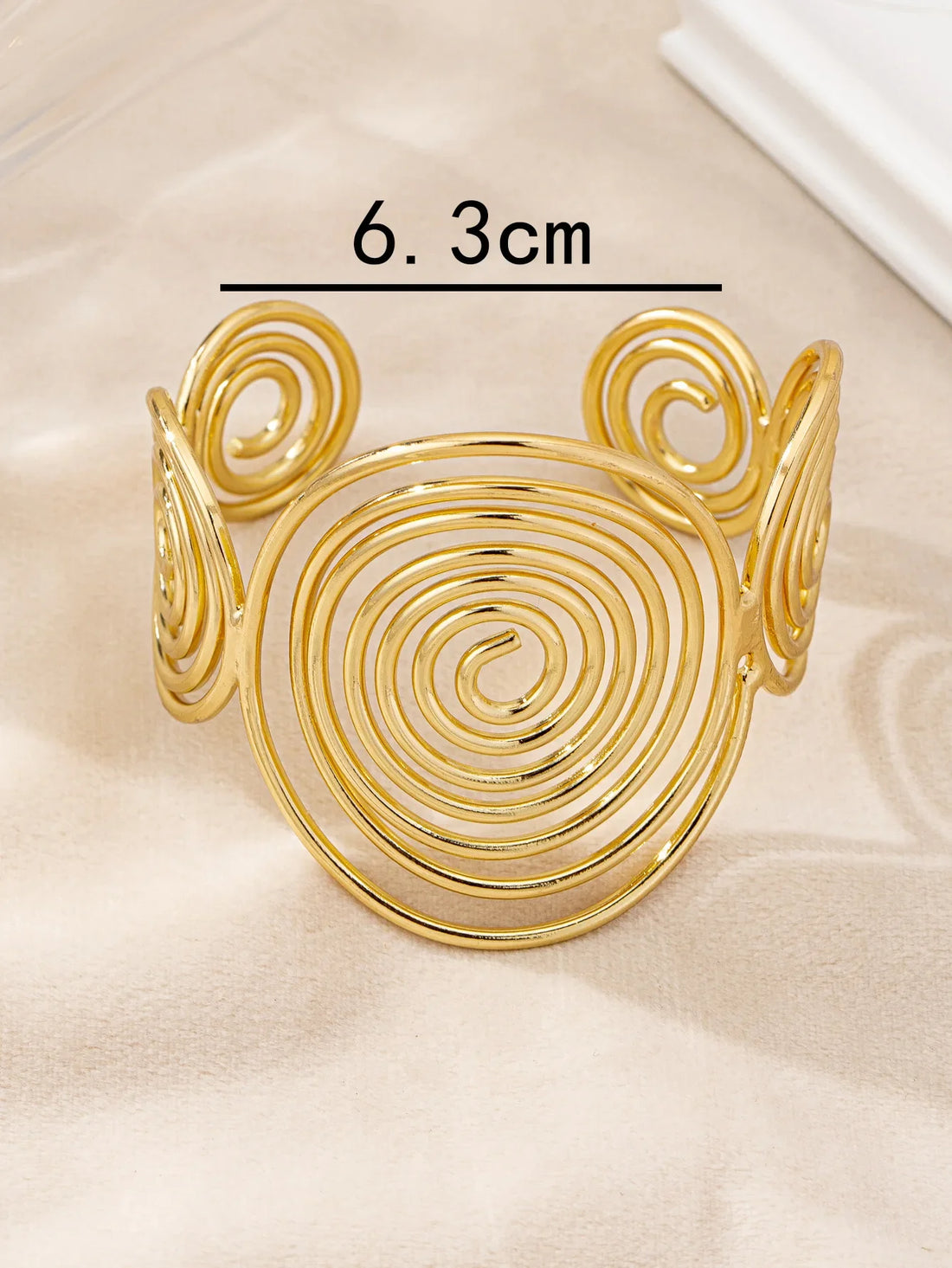 Gold swirl hair cuff with 6.3 cm diameter, shown with measurement on a light fabric surface.