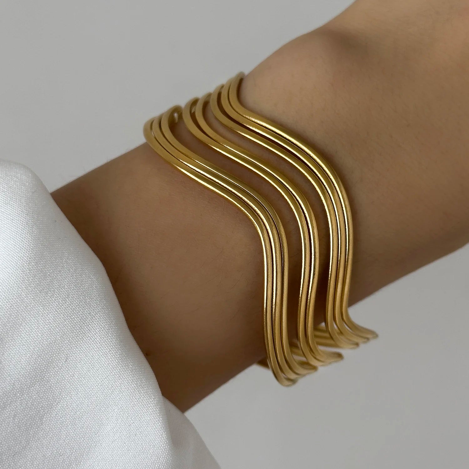 Close-up of a woman wearing a gold layered wave cuff bracelet, showcasing its elegant fluid shape
