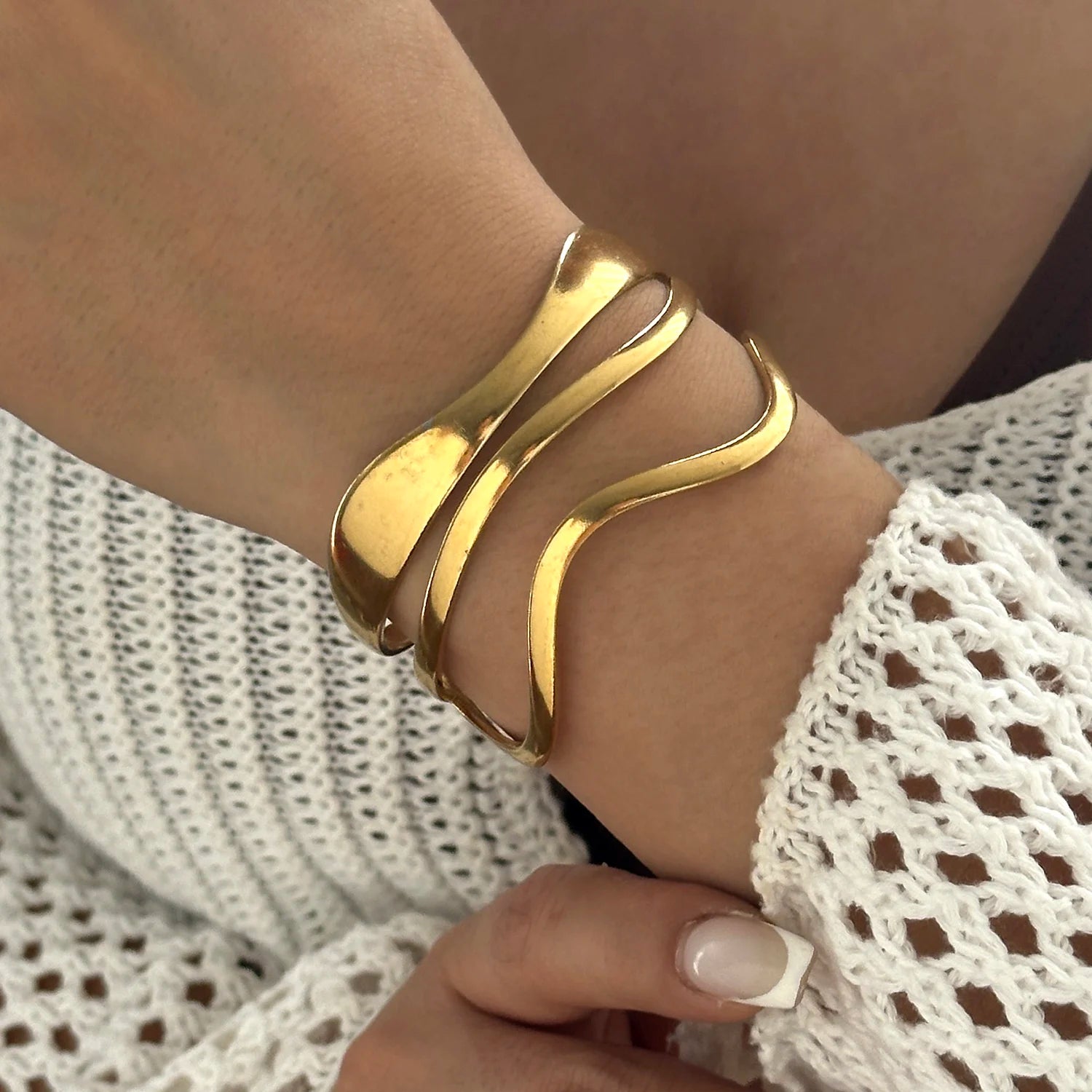 Gold wavy cuff bracelet with fluid curved design, worn on wrist for a chic minimalist style.