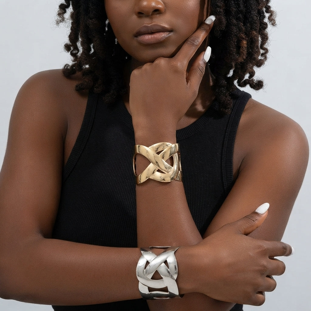 Woman in a black ribbed tank top wearing a gold interlocking-loop cuff on one wrist and a silver one on the other.