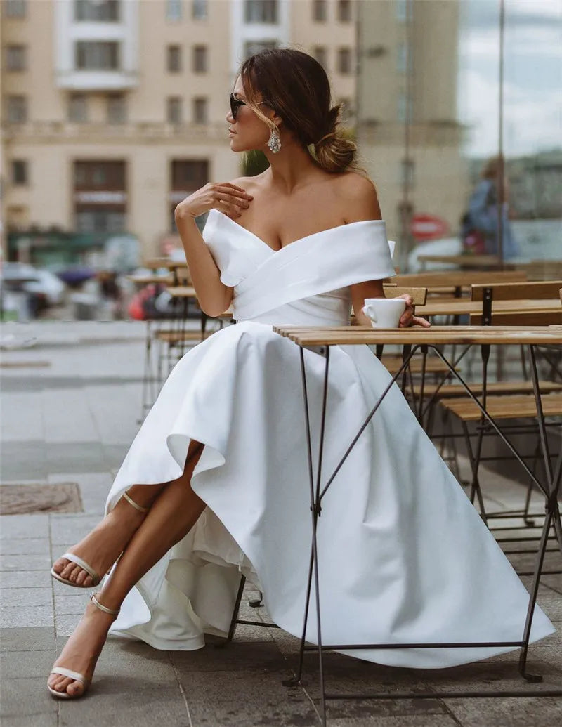 Woman in a white off-shoulder dress sitting at an outdoor cafe table.