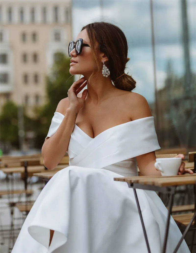 Woman in a white off-shoulder dress sitting at an outdoor cafe table.