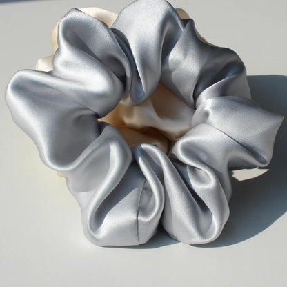 Woman with dark hair wearing a silver mulberry silk scrunchie in a low bun. Stylish and gentle silk hair tie for a sleek, elegant look.