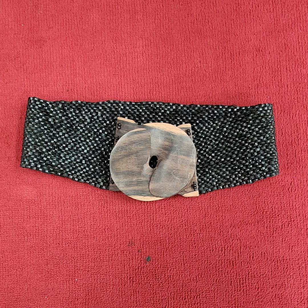 Handcrafted vintage woven fabric belt with a wooden buckle, displayed on a red background. Unique and elegant fashion accessory for women.