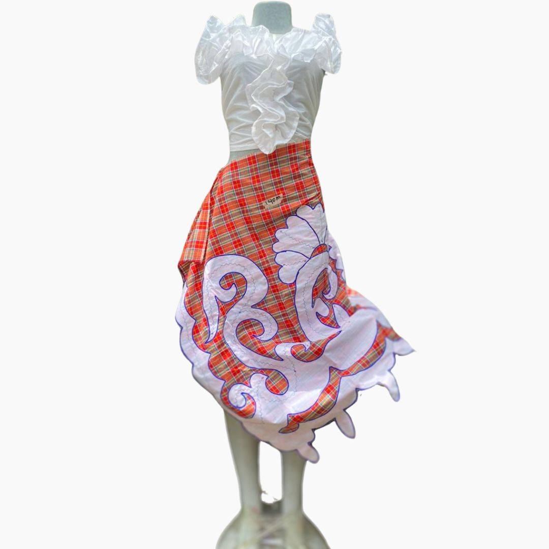 Traditional Surinamese pangi wrap skirt with vibrant orange plaid and intricate white embroidery, paired with a ruffled white blouse. Perfect for cultural celebrations.