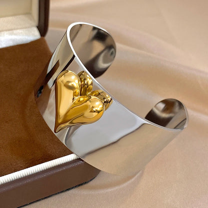 Wide silver cuff bracelet with layered golden heart detailing displayed inside a jewelry box.