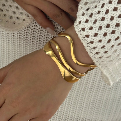 Woman wearing a gold geometric cuff bracelet with fluid wavy lines, showcasing elegant fit