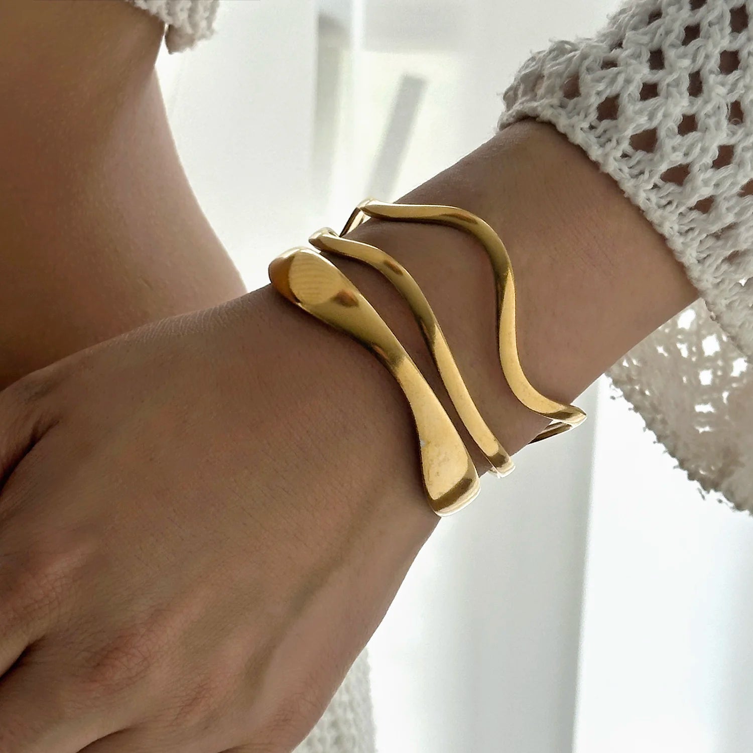 Woman wearing a gold geometric cuff bracelet with fluid wavy lines, showcasing elegant fit