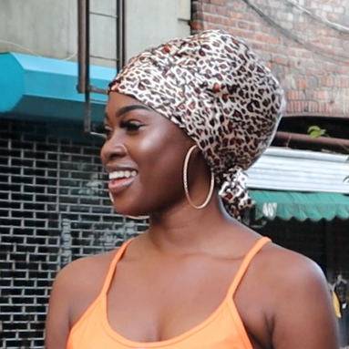 Woman wearing a leopard print headscarf and orange tank top outdoors.