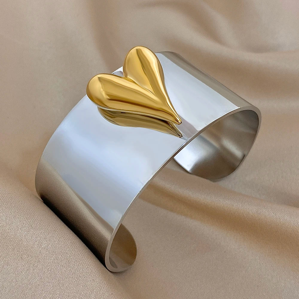 Smooth silver cuff bangle with a centered gold heart design on a reflective wide band.