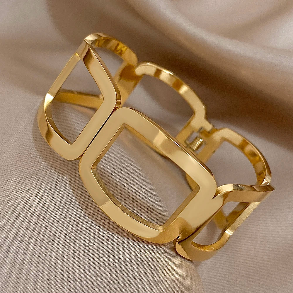 Gold geometric cuff with polished open frames and a hinge, on champagne satin