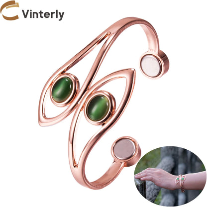 A rose gold butterfly-shaped open bangle bracelet with two green cabochon gemstones, shown on a white background with a brand logo &