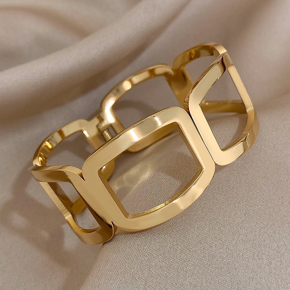 Gold open-frame link cuff with a visible hinge and spring detail, on soft fabric