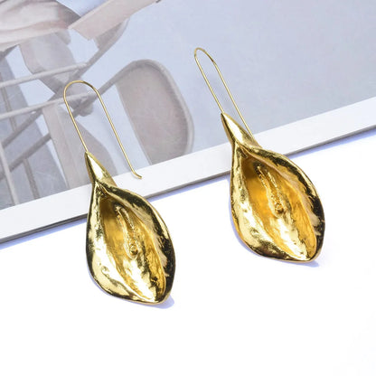 Gold teardrop earrings on a reflective surface with a blurred background