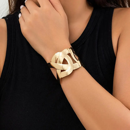 Wrist wearing a gold open cuff with interlocking loop cutouts, with a black ribbed top.