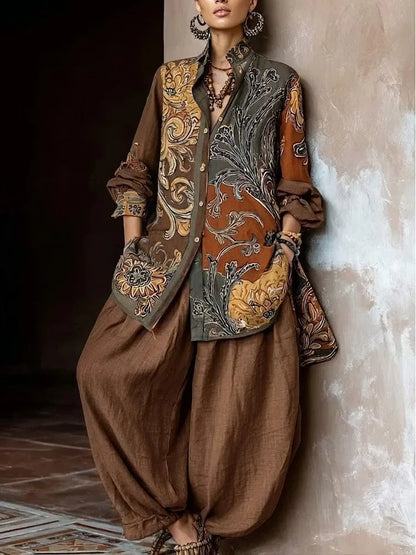 A model wearing a bohemian-style outfit consisting of brown harem pants, a brown shirt, and a matching embroidered vest with intricate floral and scroll patterns in gold, orange, and gray, leaning against a textured wall.