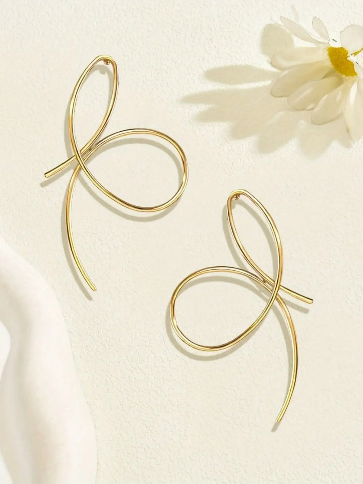 Gold bow-shaped earrings on a light background with a white flower.