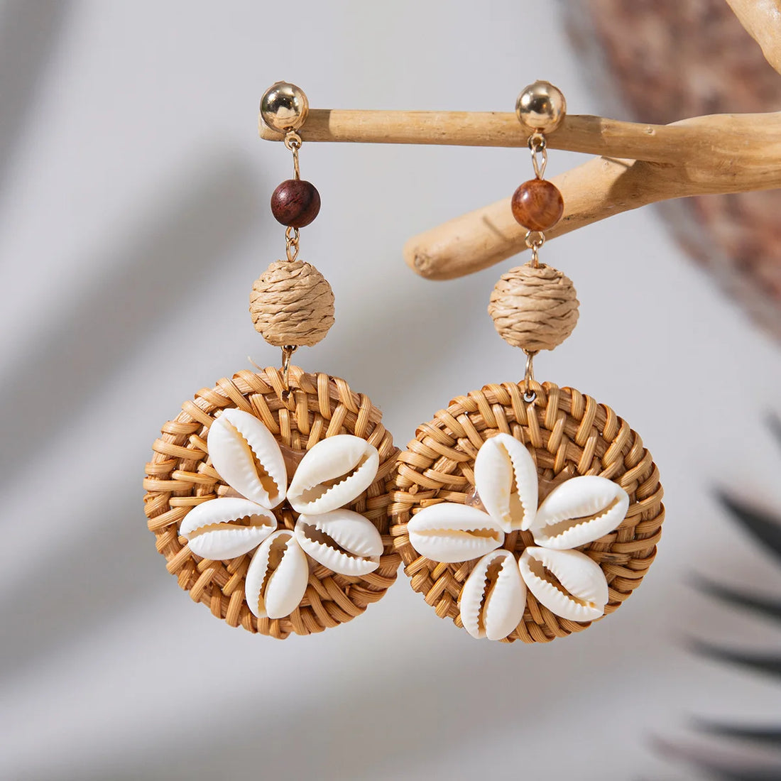 Pair of earrings with woven design and shell-like centers on a wooden stick.