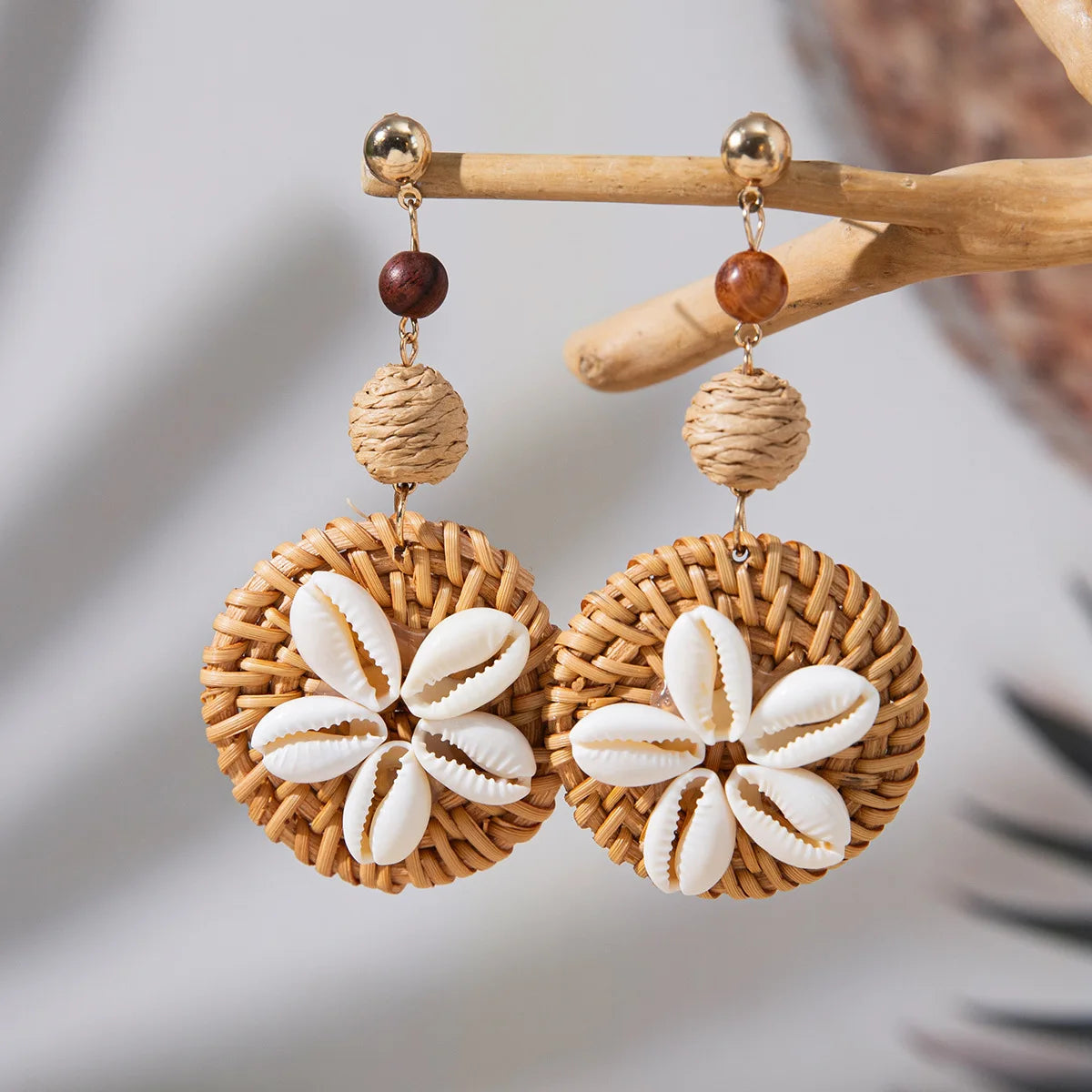 Pair of earrings with woven design and shell-like centers on a wooden stick.