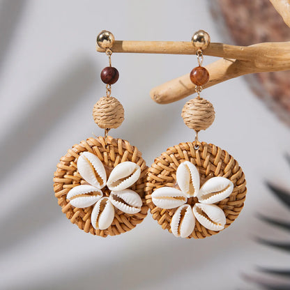 Pair of earrings with woven design and shell-like centers on a wooden stick.