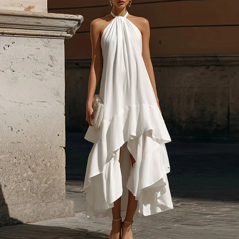 Woman wearing a white halter neck dress with ruffled layers, standing against a stone wall.