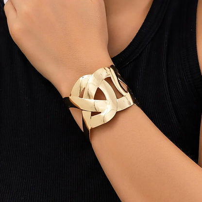 Wrist wearing a polished gold open cuff with interlocking loop cutouts, with a black ribbed top.