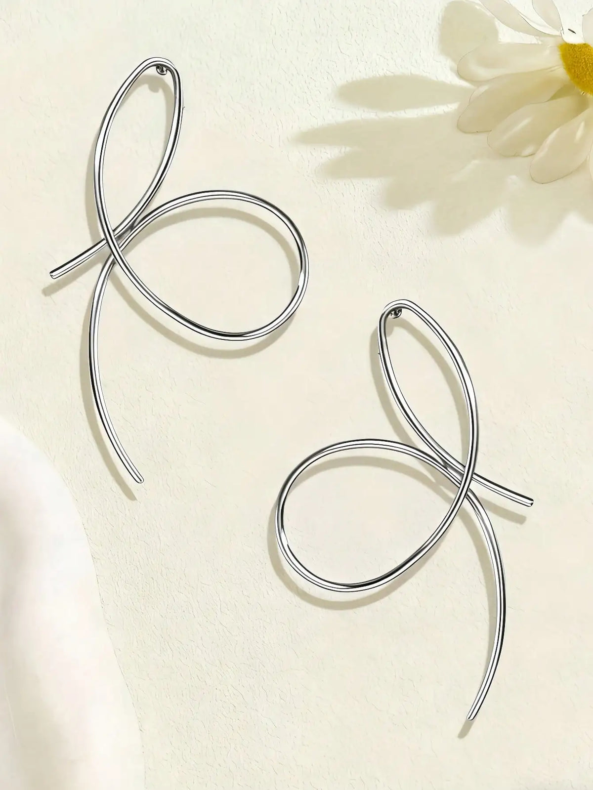 Silver bow-shaped earrings on a light background with a flower.