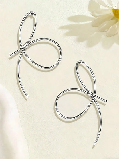 Silver bow-shaped earrings on a light background with a flower.
