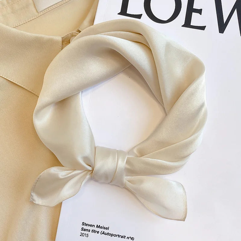 Beige silk scarf tied in a knot on a white surface with &