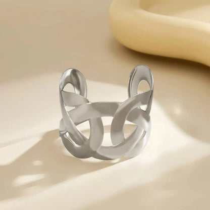 Silver open cuff with interlocking looped cutouts, standing on a cream surface with soft shadows.