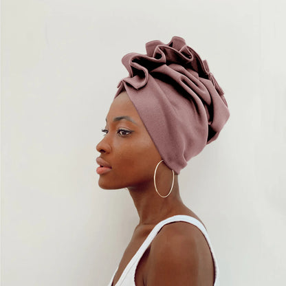 Woman wearing a mauve headscarf with ruffled details on a plain background