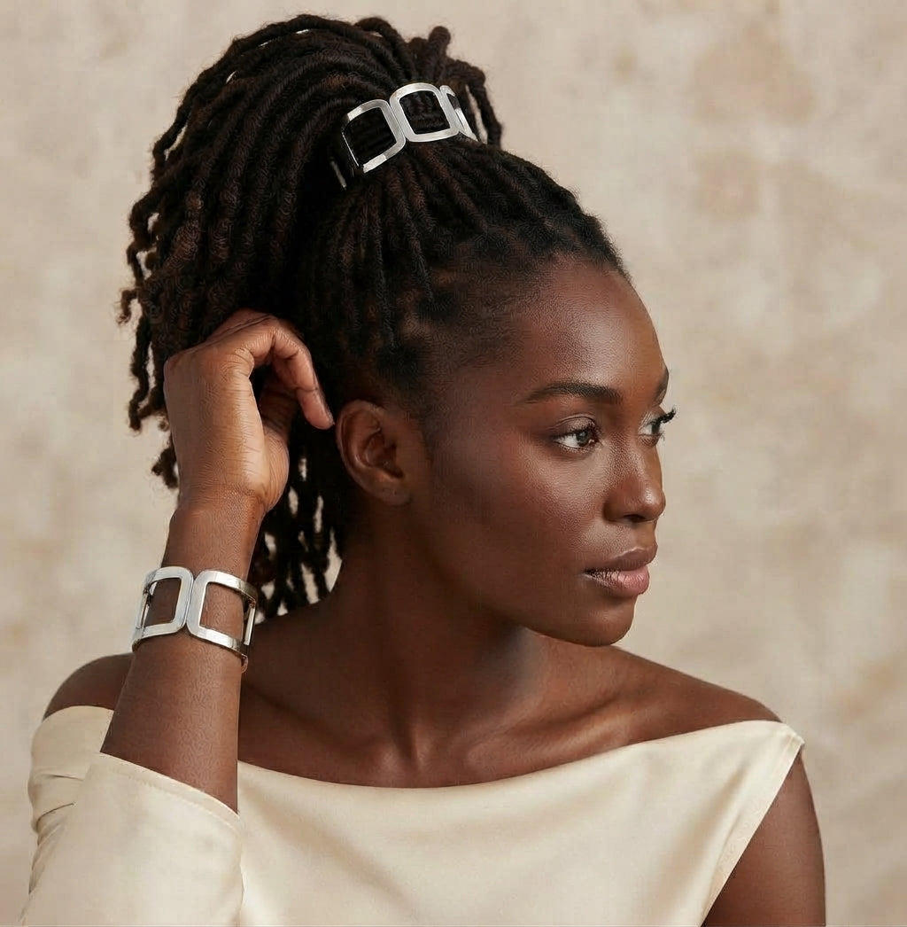 Woman with locs in a high ponytail wearing a silver geometric link hair cuff, with a matching silver cuff on her wrist
