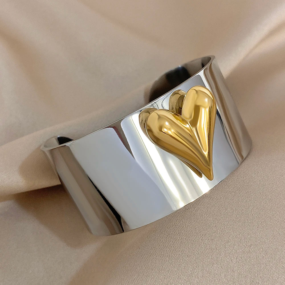 Wide silver cuff bracelet featuring a raised gold puffy heart design on a smooth reflective surface.