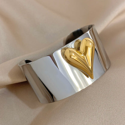 Wide silver cuff bracelet featuring a raised gold puffy heart design on a smooth reflective surface.