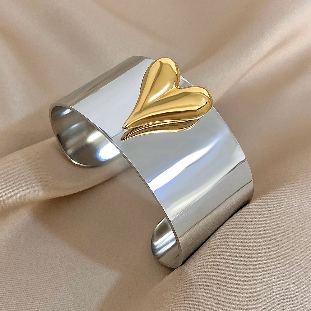 Shiny silver stainless steel cuff bracelet decorated with a raised gold sculpted heart on the front.