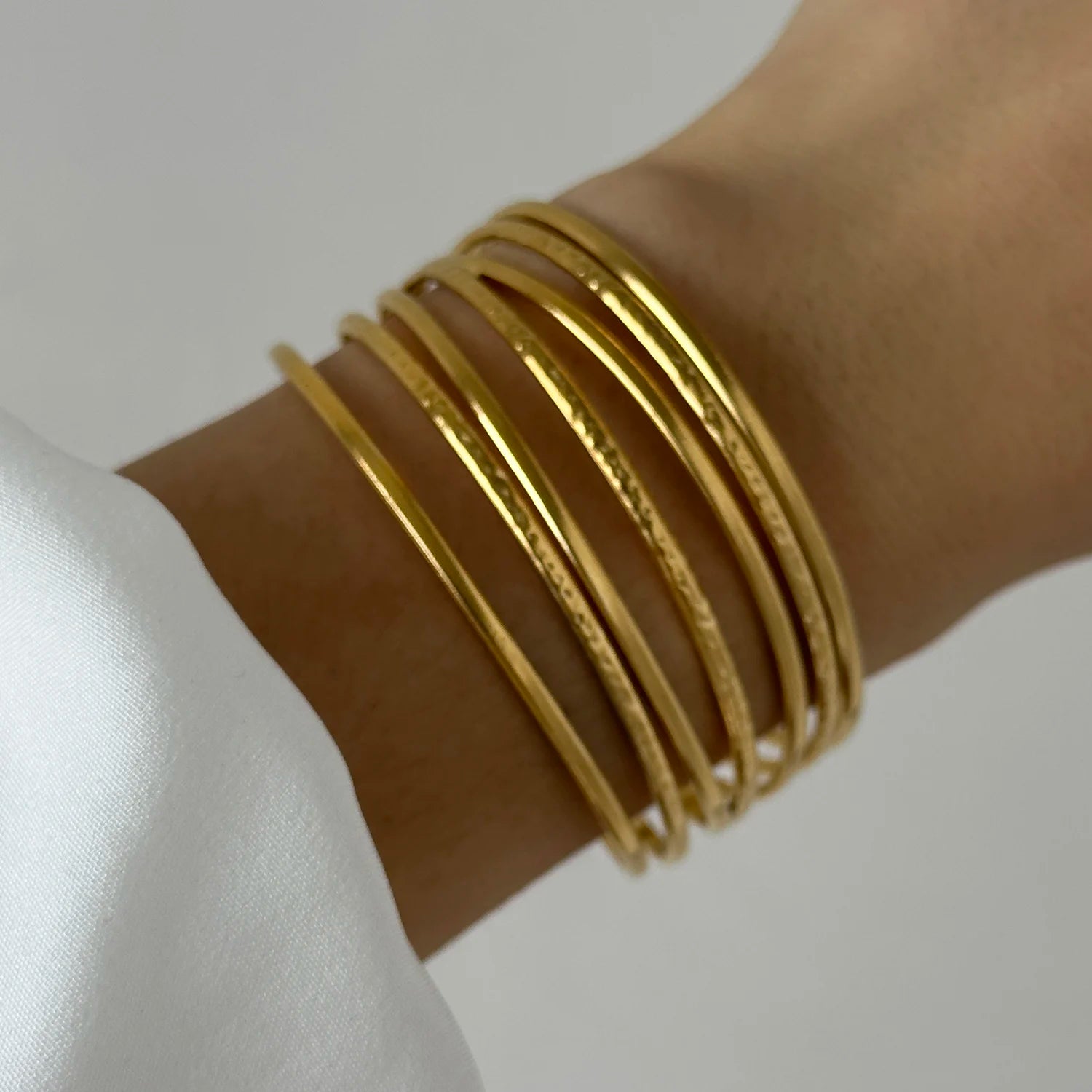 Elegant stacked gold bangles layered on wrist, showcasing a thin minimalist cuff bracelet style