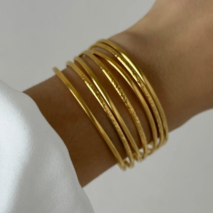 Elegant stacked gold bangles layered on wrist, showcasing a thin minimalist cuff bracelet style