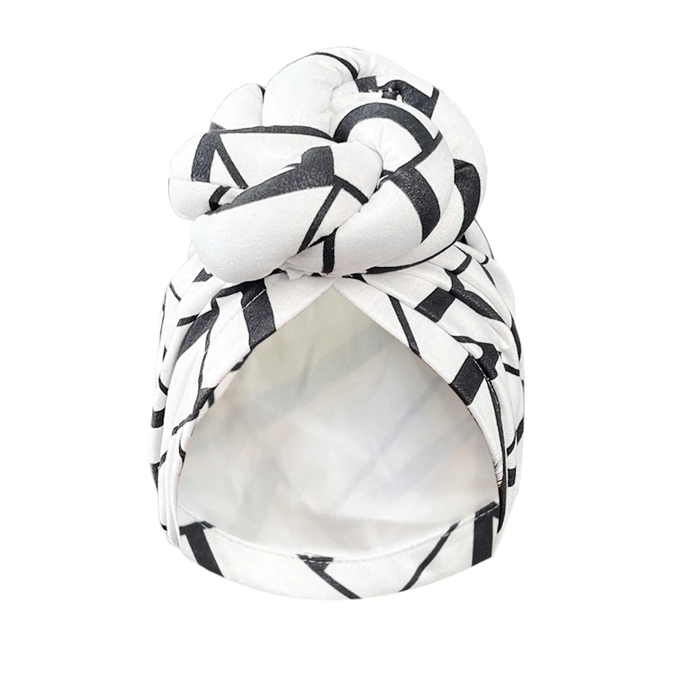 White and black geometric patterned knot turban headwrap with a stylish twisted knot. Soft and breathable fabric for a fashionable look.