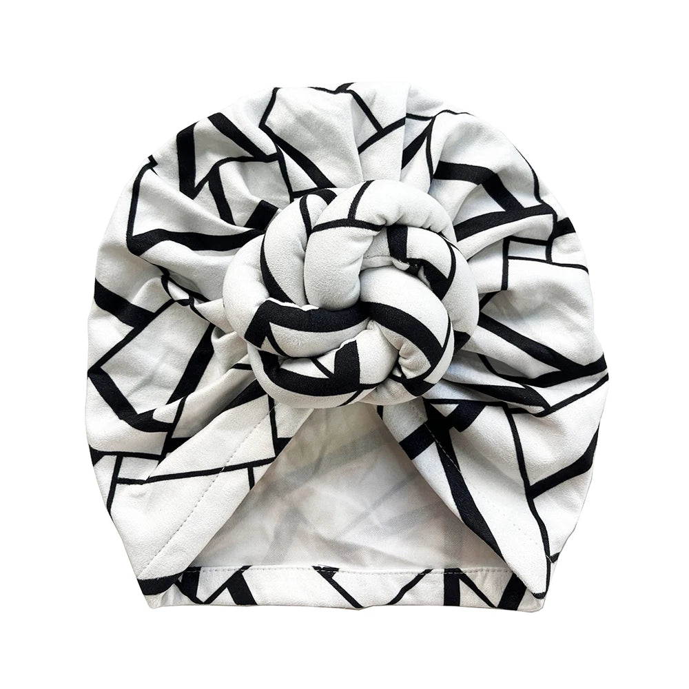 Top view of a black and white geometric patterned knot turban headwrap. Features a stylish twisted knot for a fashionable and elegant look.