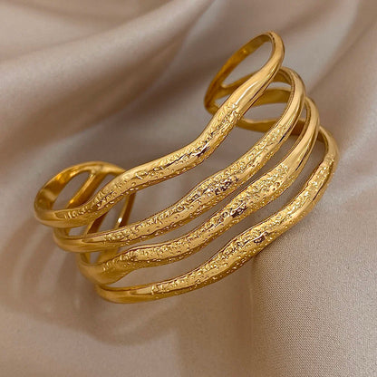 
Close-up of a gold cuff bracelet featuring textured wavy layered bands, shown with measurement lines